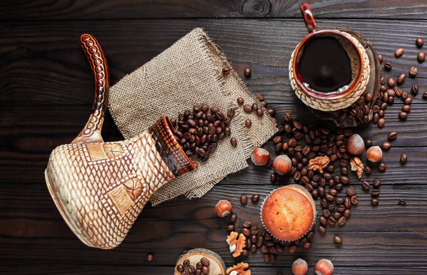 hot fragrant coffee in a vintage clay cup and coffee beans with nuts on a dark wooden background - Foto, imagen