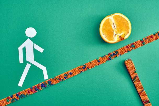 Ein Mann aus weißem Papier geht an einem Masseur entlang zu einer Orange. Ansicht von oben. Gesunder Lebensstil. Motiv- und Werbefotografie. Für Entspannung und Gesundheit. - Foto, Bild
