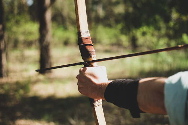 A man shoots a bow in the open air. The near foreshortening. An arrow is pulled over the bow. - Photo, Image
