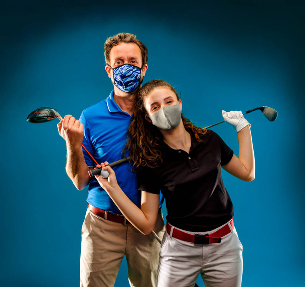 Közelkép egy lány és egy fiú pózol koronavírus maszk és golf klubok, mielőtt játszani kezd - Fotó, kép