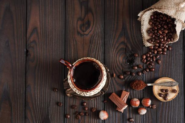 hot fragrant coffee in a vintage clay cup and coffee beans with nuts on a dark wooden background - Foto, imagen