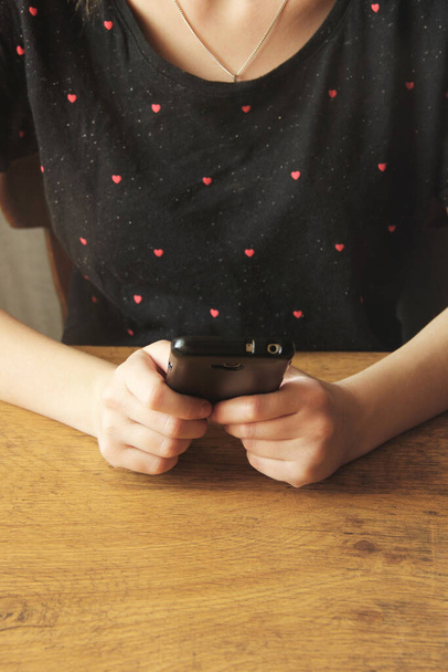 Black phone in the hands of a girl in a black T-shirt - Φωτογραφία, εικόνα