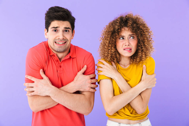 Portrait of displeased frozen caucasian people man and woman wearing t-shirts shaking and trembling from cold isolated over violet background - Photo, Image