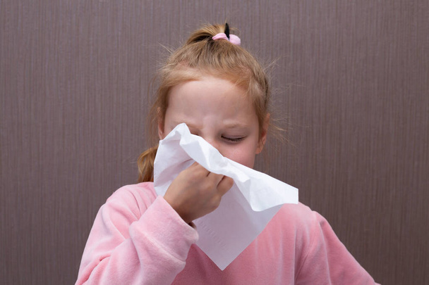 little girl has a runny nose and blows her nose into a paper handkerchief. - Photo, Image
