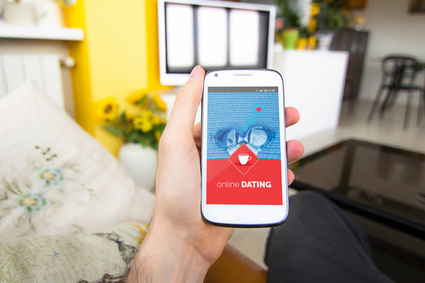 Junger Mann zu Hause mit Handy und Online-Dating-App auf dem Bildschirm. Menschen treffen und Liebe online finden. - Foto, Bild