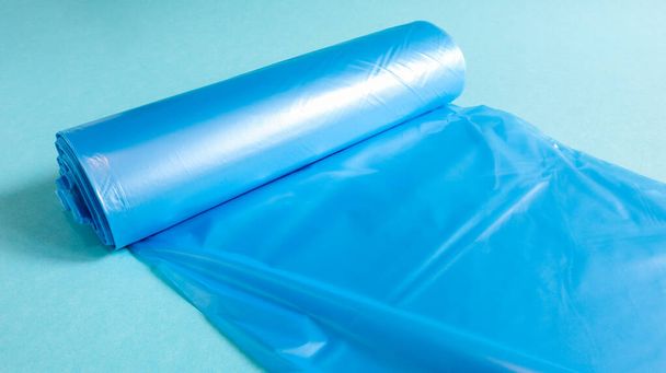 Ένα ρολό από πλαστικές σακούλες σκουπιδιών σε μπλε χρώμα σε μπλε φόντο. Τσάντες που έχουν σχεδιαστεί για να φιλοξενούν σκουπίδια σε αυτά και χρησιμοποιούνται στο σπίτι και τοποθετούνται σε διάφορα δοχεία απορριμμάτων - Φωτογραφία, εικόνα