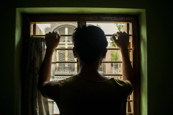 tył sylwetka zdjęcie mężczyzna facet patrząc na zewnątrz z okna trzymając pręty okienne - Zdjęcie, obraz