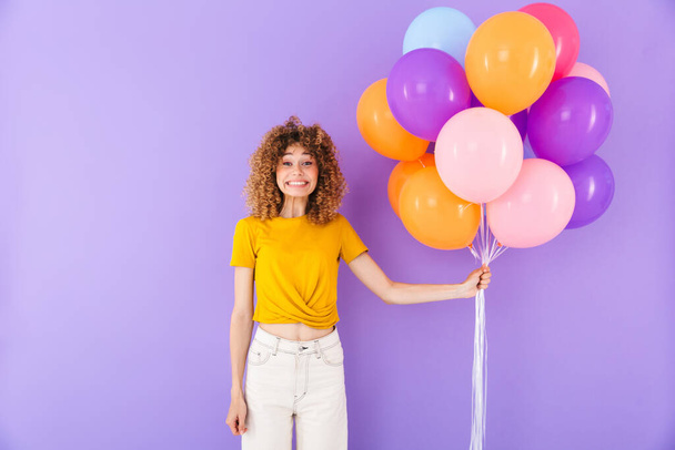 Image gros plan de heureuse femme enchantée riant tout en posant dans des ballons à air multicolores isolés sur fond violet
 - Photo, image