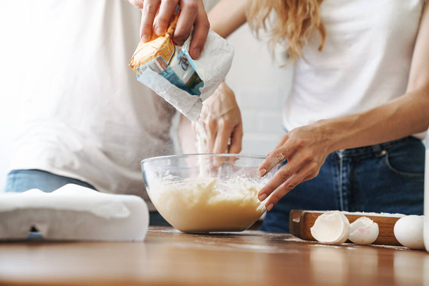 Cropped image of lovely couple cooking breakfast and mixing dough in kitchen at home - Zdjęcie, obraz