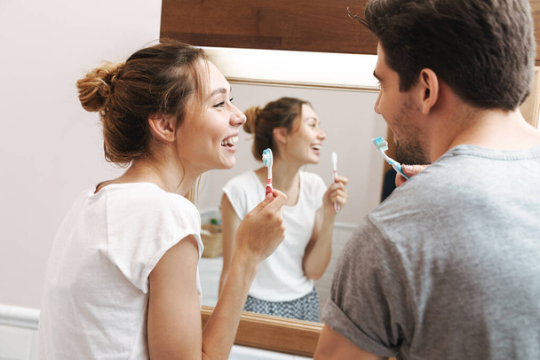 Image of caucasian couple smiling while cleaning teeth together in bathroom with brush and toothpaste - Foto, Bild
