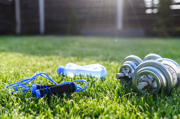 Dumbbells, bottle of water and jump rope on grass - Foto, imagen