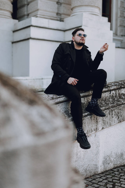Full length of stylish guy in sunglasses resting in the city while smoking - Photo, Image