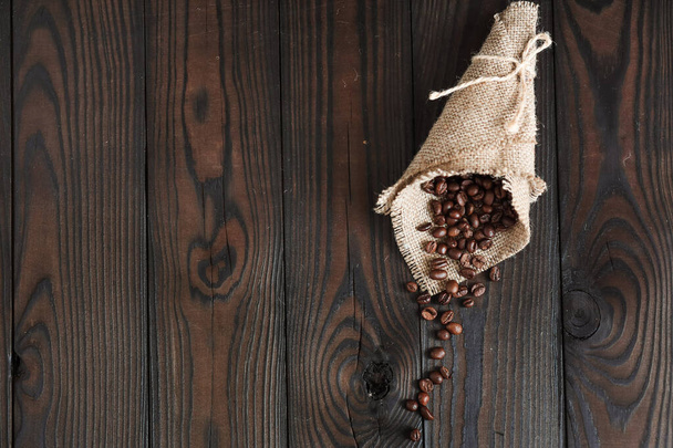 Roasted aromatic coffee beans on burlap, ground coffee in a spoon, on a dark wooden background - Foto, imagen