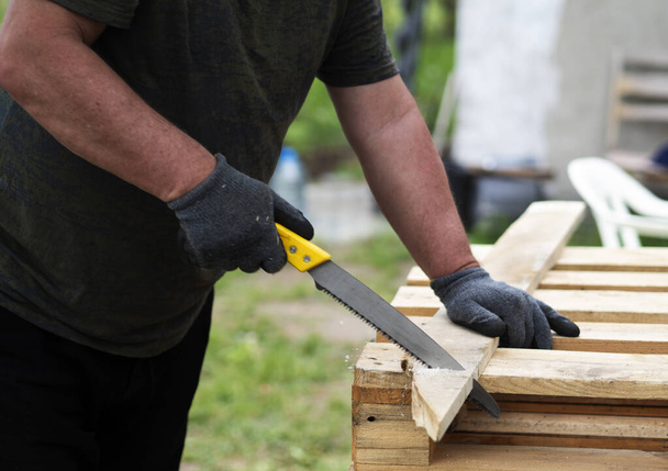 Hands of a caucasian man sawing a pine board in the garden - Фото, зображення