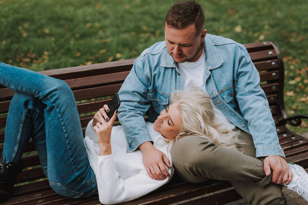 Вид зверху гарненька блондинка використовує мобільний телефон, відпочиваючи зі своїм чоловіком на лавці провулок
 - Фото, зображення