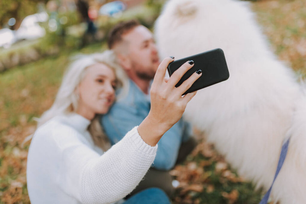 Mutlu çift akıllı telefon kullanırken ve selfie çekerken parkta vakit geçiriyor. - Fotoğraf, Görsel