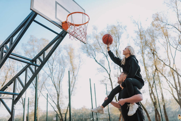 Homme et femme souriants jouant à des jeux sur le terrain de basket pendant la journée ensoleillée
 - Photo, image