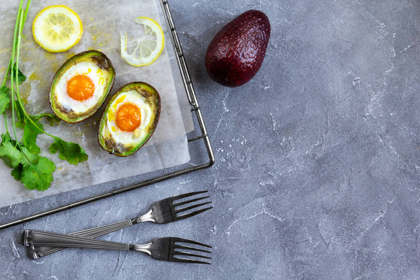 Keto dieetgerecht: gebakken avocado Boten met eieren, citroen en koriander op bakpapier. Grijze achtergrond, Kopieerruimte - Foto, afbeelding
