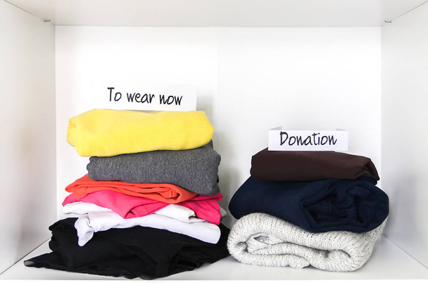 Kleidersortierung im heimischen Kleiderschrank zum Tragen und Spenden. verschiedene Kleidungsstücke auf weißem Regalhintergrund - Foto, Bild