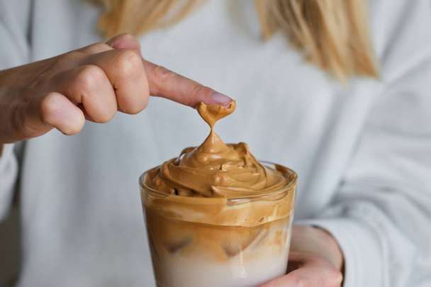 Dalgona coffee. Cold drink with ice. Whisk instant coffee, sugar and add in milk. Glass of coffee in girl hand. Woman barista making delicious summer beverage. Professional service - Zdjęcie, obraz