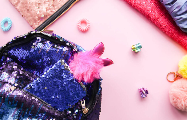 Φωτεινή σύνθεση αξεσουάρ μόδας και φόρεμα. Glitter πούλιες sweetshot, τσάντα, σακίδιο, πολύχρωμα pompons και ταινίες για τα μαλλιά. Διαφορετικά αντικείμενα σε μαλακό ροζ παστέλ φόντο. Επίπεδο lay, πάνω όψη. - Φωτογραφία, εικόνα