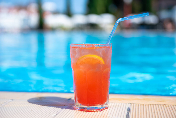 Fresh alcoholic red cocktail sex on beach with ice in glass on edge of pool in summer weather against background washed up pool and recreation area. Concept good holiday and travel, place for text. - Foto, Bild