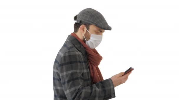 Adult man wears protective medical mask talking on the phone and walking on white background. - Video