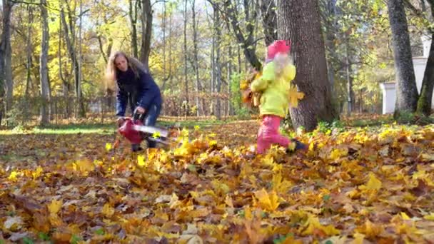 vrouw en haar dochtertje meisje spelen met kleurrijke herfst bladeren in tuin - Video