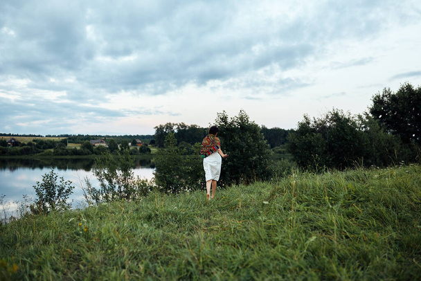 A girl runs along a lush green field to a pond - Foto, immagini
