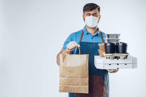 Delivery man in protective mask and medical gloves holding takeaway food. Compliance with the hygiene rules while covid-19 pandemic - Φωτογραφία, εικόνα