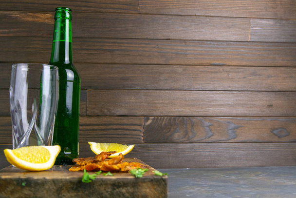 Szárított sügér sörrel, citrommal és burgonyaszirmokkal sötét fa táblán. Sörrel rágcsálni a halat. Elülső nézet szabad terekkel. - Fotó, kép