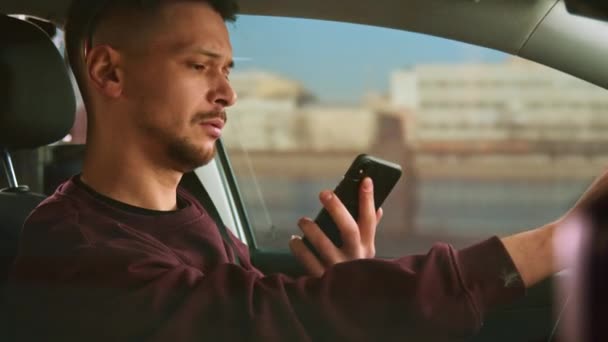 Een aantrekkelijke man met een kort kapsel rijdt de auto met één hand en spreekt aan de telefoon. - Video