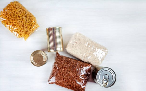 humanitarian assistance for poor and large families. Donation during crisis, pandemic or quarantine. Tin cans, canned food, stew, buckwheat, rice and pasta in transparent bags on white background. - Zdjęcie, obraz