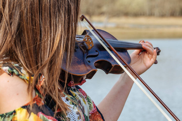 Het meisje speelt viool. Meisje en viool op een achtergrond van water. Het meisje heeft een viool. Het meisje en de oude viool.   - Foto, afbeelding