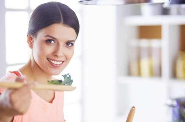 Smiling young woman mixing fresh salad in the kitchen. - Foto, Imagem