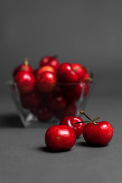 Selective focus, photograph of a glass container full of cherries, on a dark grey background. - Φωτογραφία, εικόνα