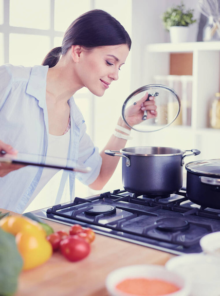 Young woman standing by the stove in the kitchen - Foto, Imagen