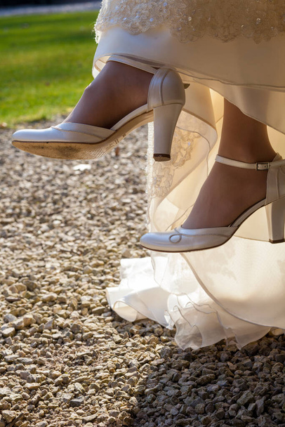 Μια νύφη κάθεται σε μια καρέκλα έξω, στα πόδια νύφες υπάρχουν σχεδιαστής ψηλοτάκουνα παπούτσια - Φωτογραφία, εικόνα