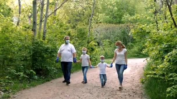 Aile: Baba, anne, oğul ve kız tıbbi maskeler, beyaz tişörtler ve lastik eldivenlerle parkta yürüyorlar. Covid-19 koronavirüs enfeksiyonlarından korunma kavramı. - Video, Çekim