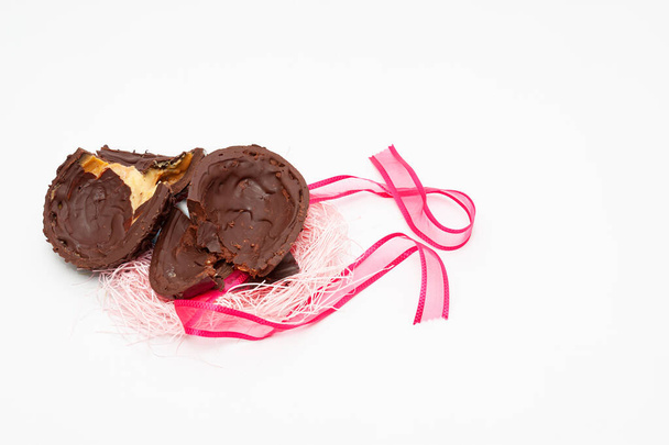 Zelfgemaakt gebroken chocolade ei met rood lint. Viering van Pasen, Moederdag en Valentijnsdag. Geïsoleerd op witte achtergrond. Kopieerruimte. - Foto, afbeelding