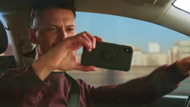 Atrakcyjny mężczyzna prowadzi samochód i kręci wideo bloga na smartfonie. - Materiał filmowy, wideo