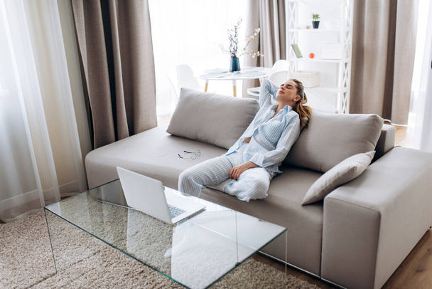 Уютное утро выходных. Молодая привлекательная девушка в пижаме расслабляется дома на удобном диване
 - Фото, изображение
