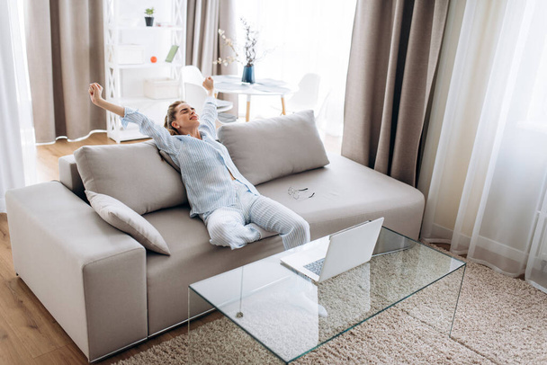 Затишні вихідні вранці. Молода приваблива дівчина в піжамі відпочиває вдома на зручному дивані
 - Фото, зображення