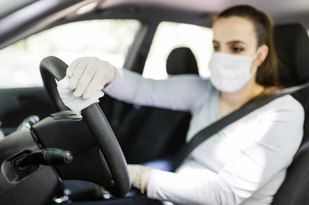 Female driver using wet wipe for disinfecting car steering wheel against coronavirus disease. - Foto, Bild