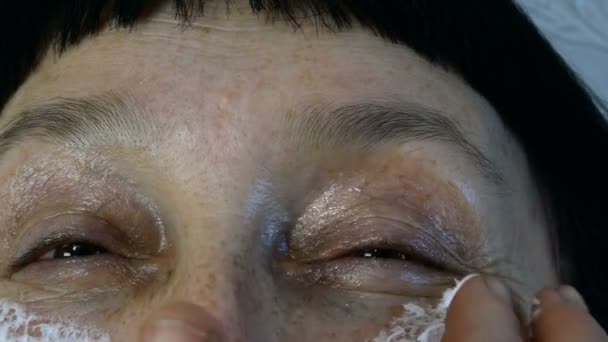 Volwassen volwassen vrouw, blanke etniciteit smeren hydraterende cosmetische crème rimpels op haar gezicht met vingers, op zoek naar camera. Close-up. - Video