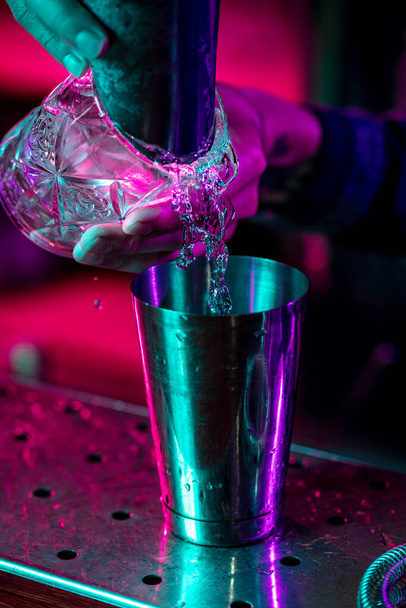 Close up of barman finishes preparation of alcoholic cocktail, pouring drink in multicolored neon light - Photo, image