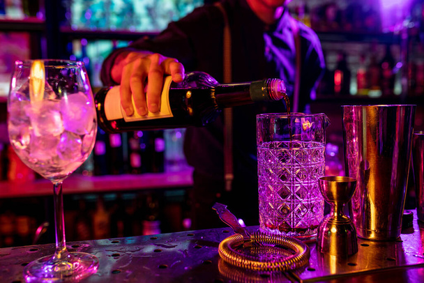 Primer plano de barman termina la preparación de cóctel alcohólico, vertiendo bebida en luz de neón multicolor
 - Foto, imagen
