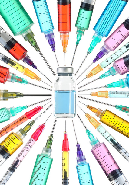 Concepto de cura de vacunas. Vial de medicamentos rodeado de jeringas coloridas con agujas apuntando hacia la vacuna
. - Foto, Imagen