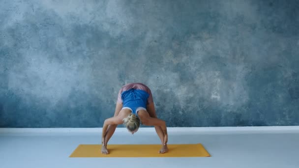 instruktor jogi pochyla się rozciągając tylne nogi szerokość ramion od siebie na macie w studio - Materiał filmowy, wideo