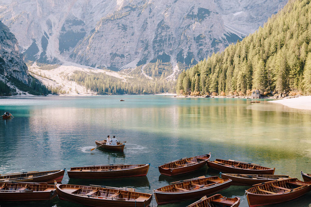 Wedding couple sailing in a wooden boat at the Lago di Braies in Italy. Newlyweds in Europe, on Braies lake, in the Dolomites. The groom rows the oars, the bride sits opposite him. - Foto, Bild